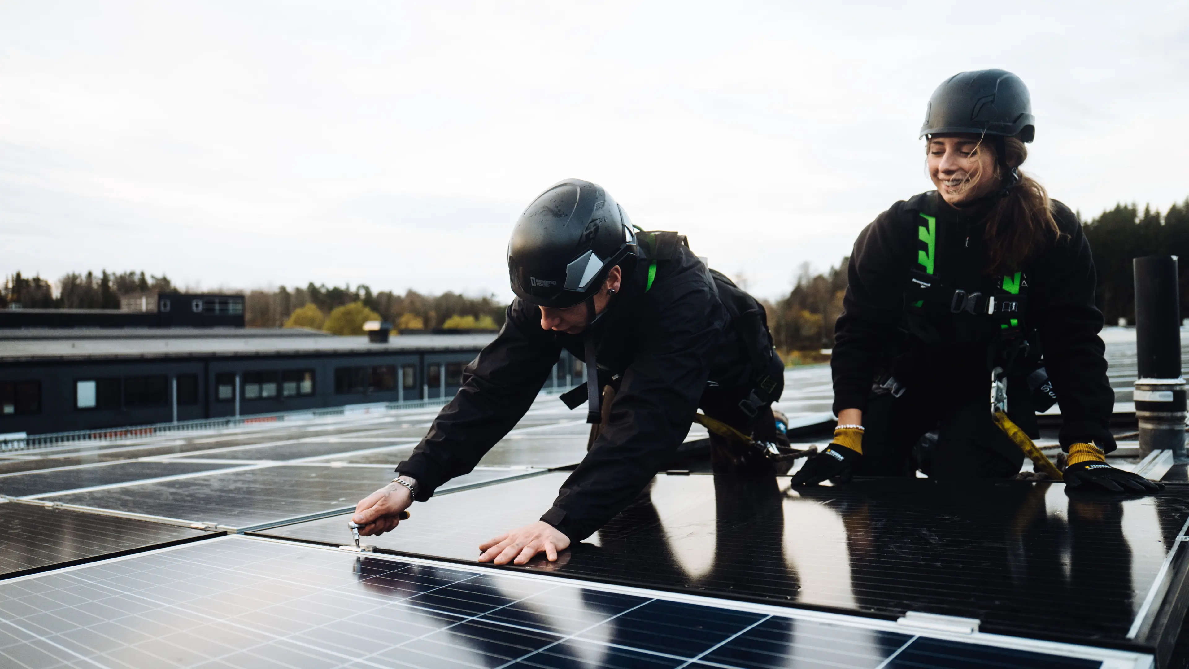 Två installatörer med skyddsutrustning monterar solceller på ett platt tak